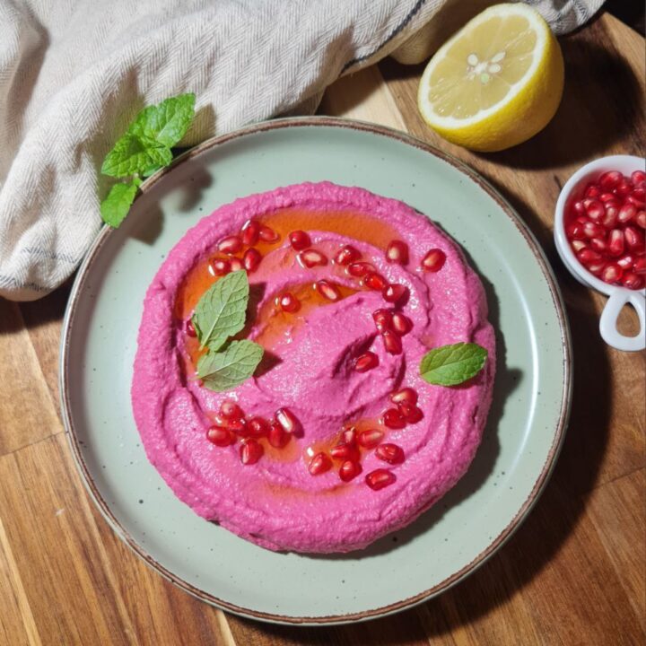 Beetroot hummus garnished with pomegranate seeds and fresh mint. A bowl of creamy beetroot hummus garnished with pomegranate seeds, olive oil, and fresh mint leaves.