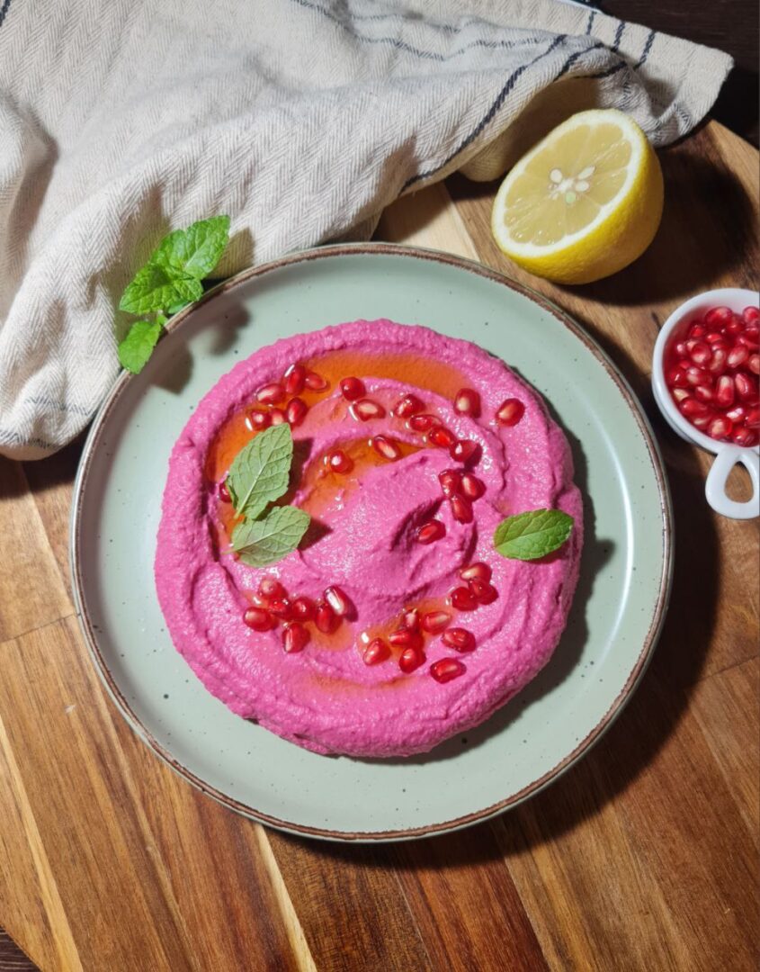 Beetroot hummus garnished with pomegranate seeds and fresh mint. A bowl of creamy beetroot hummus garnished with pomegranate seeds, olive oil, and fresh mint leaves.