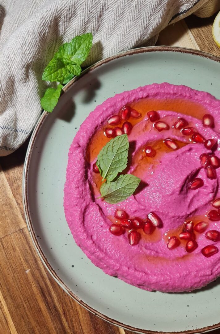 a plate of pink hummus with mint leaves and pomegranate seeds