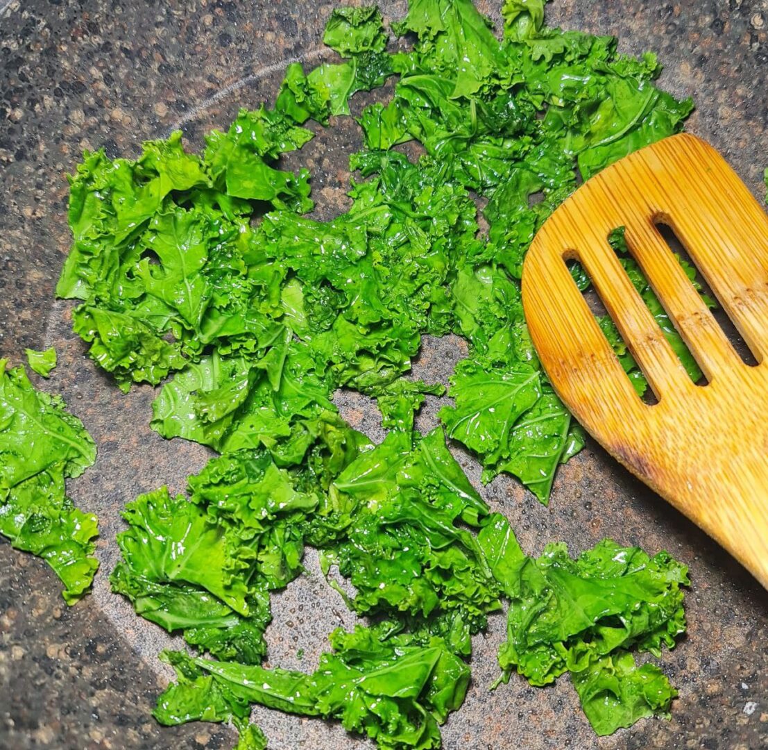 a wooden spatula and kale in a pan