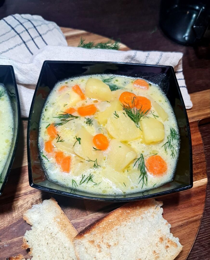 a bowl of soup with vegetables and bread on a wooden surface