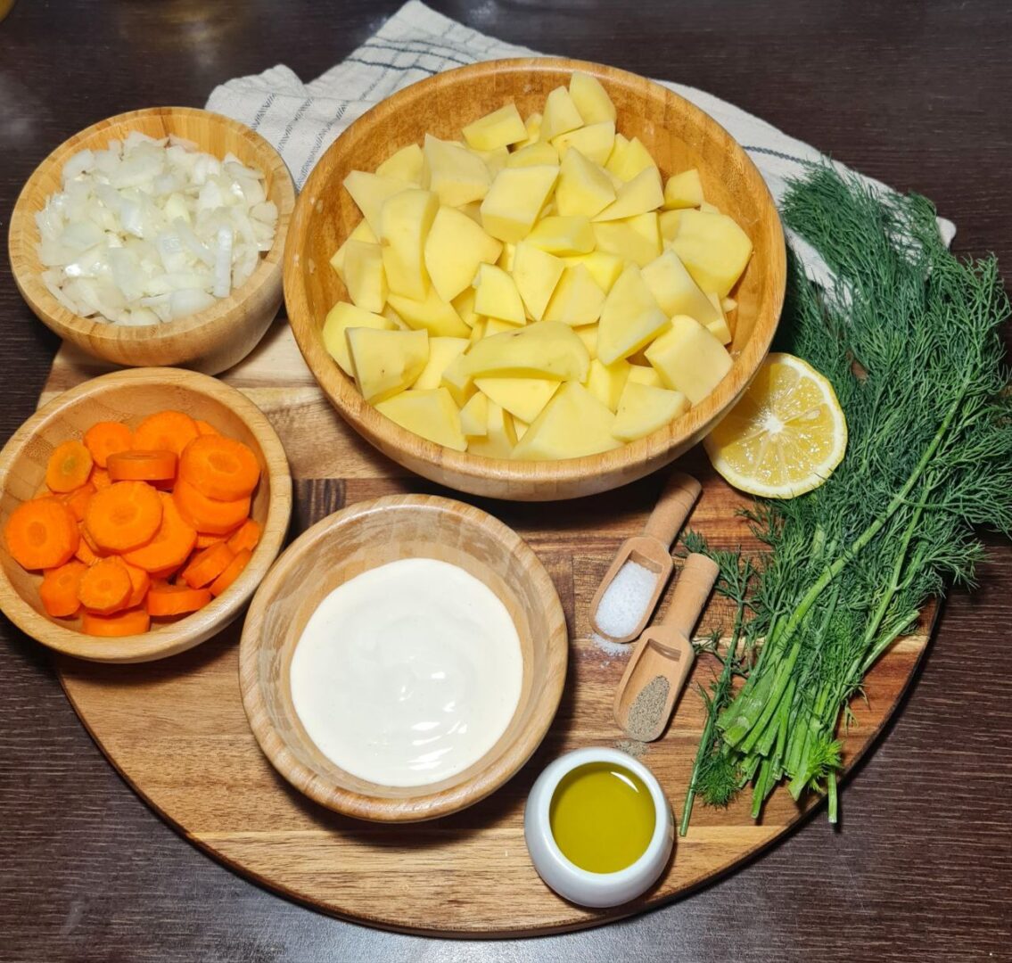 Ingredients for creamy vegan potato dill soup including chopped potatoes, carrots, onions, fresh dill, olive oil, and vegan cream. Ingredients for creamy vegan potato dill soup laid out: potatoes, carrots, onions, fresh dill, olive oil, and vegan cream.