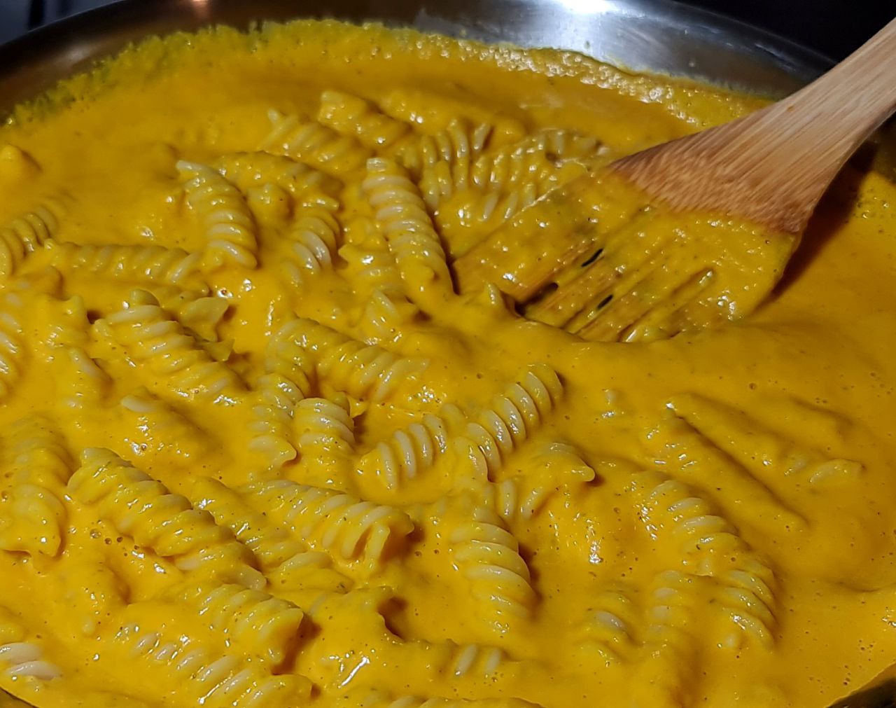 Fusilli pasta coated in creamy pumpkin sauce in a pan. Fusilli pasta simmering in a creamy pumpkin sauce.