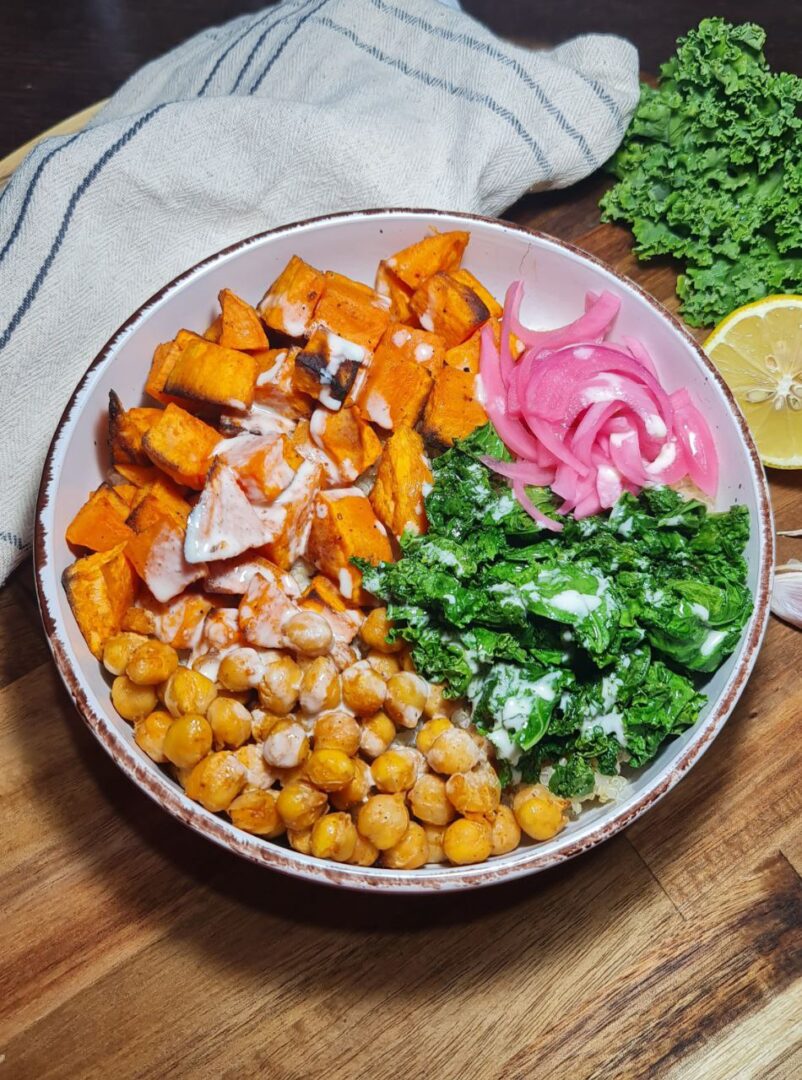 Vegan quinoa bowl with roasted sweet potatoes, chickpeas, sautéed kale, pickled onions, and tahini sauce.  A vibrant vegan quinoa bowl featuring roasted sweet potatoes, chickpeas, sautéed kale, and pickled onions drizzled with a creamy tahini sauce.