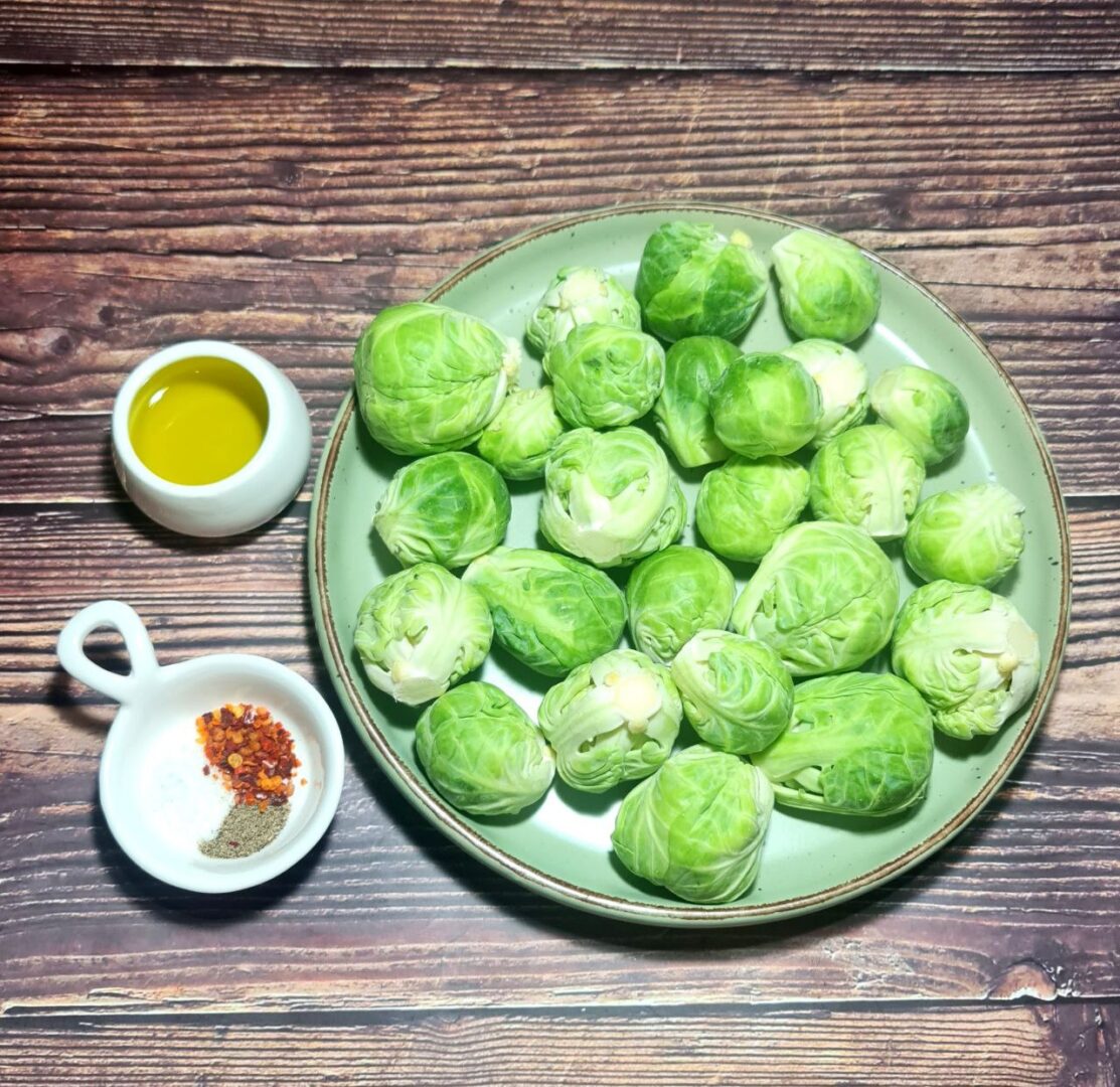 Fresh raw Brussels sprouts with olive oil and spices on a wooden table.  Fresh Brussels sprouts prepared with olive oil, salt, pepper, and chili flakes for roasting.