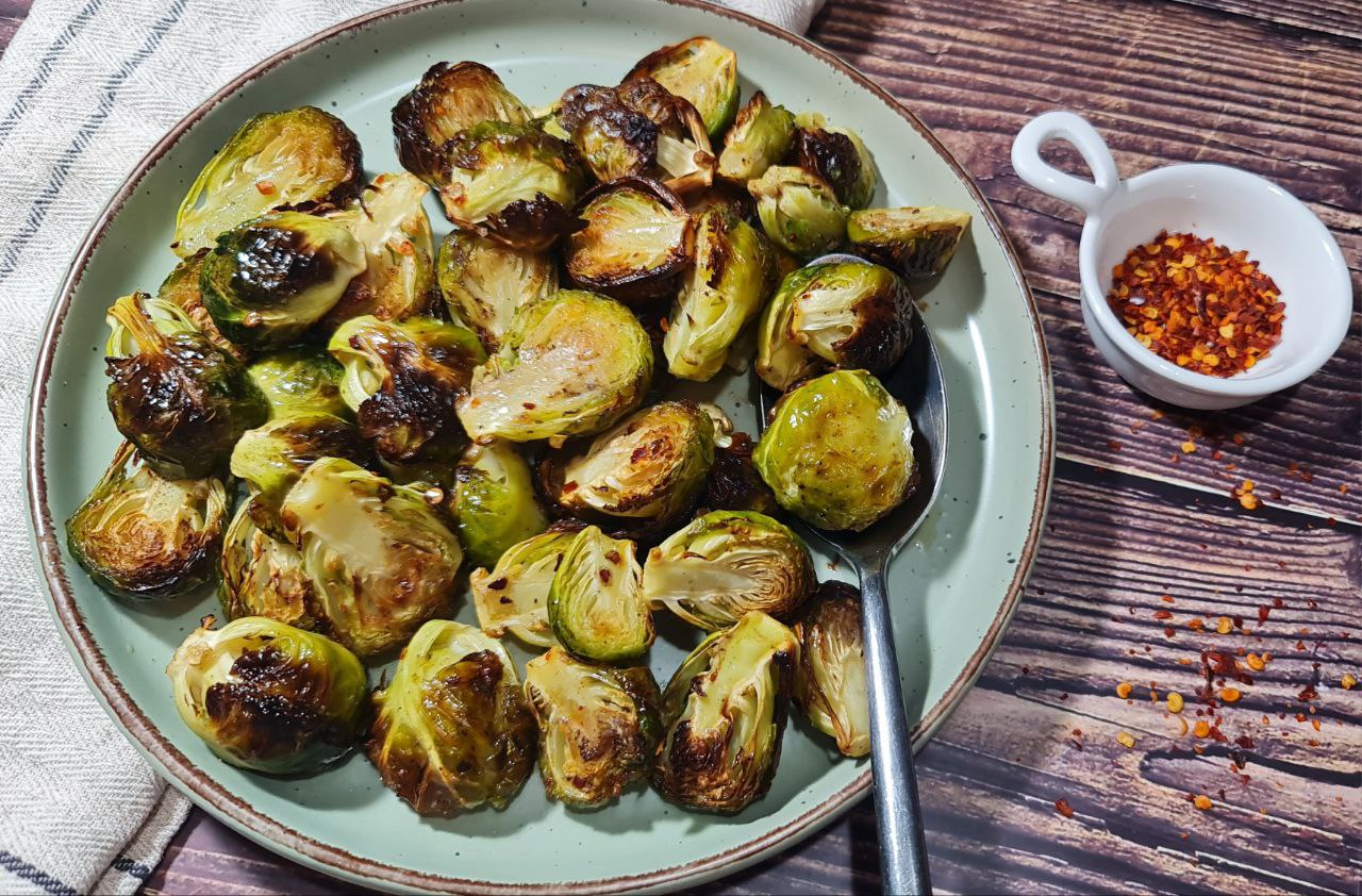 Roasted Brussels sprouts served on a plate with chili flakes on the side. A plate of perfectly roasted Brussels sprouts with a side of chili flakes.