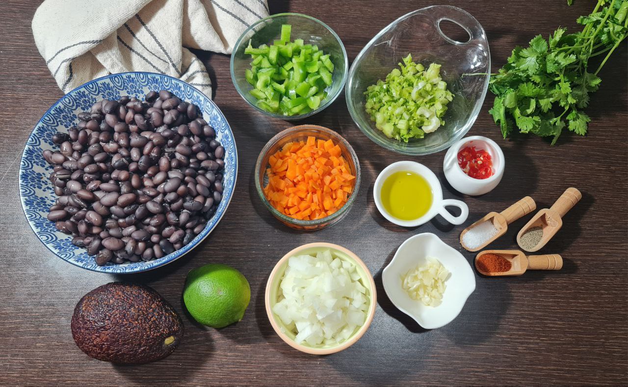 Ingredients for Spicy Black Bean Soup including black beans, chopped vegetables, avocado, lime, spices, and olive oil. Fresh ingredients for a hearty Spicy Black Bean Soup with a citrus twist.