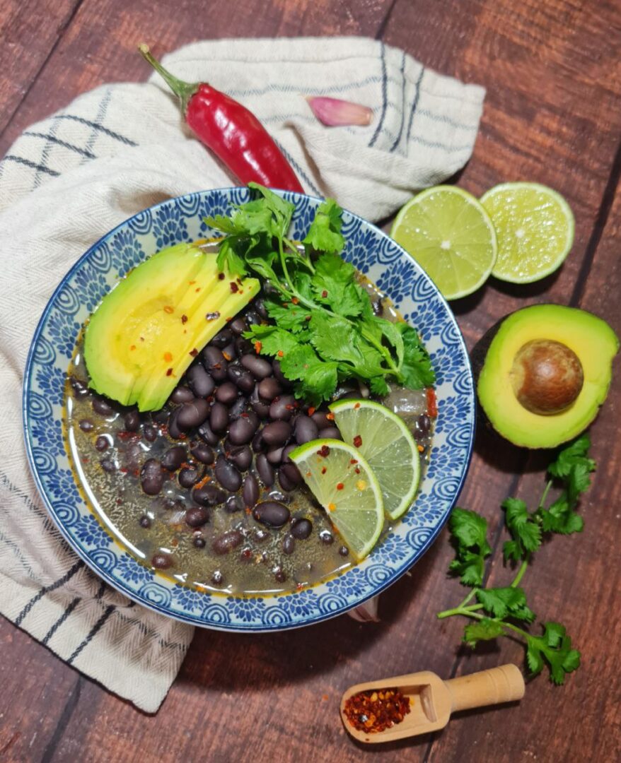 A bowl of Spicy Black Bean Soup garnished with avocado slices, cilantro, and lime wedges. A comforting bowl of Spicy Black Bean Soup, topped with avocado, lime, and fresh cilantro.