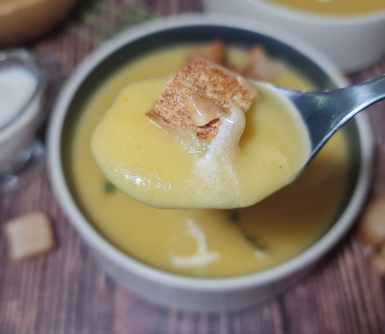 Spoonful of vegan creamy roasted garlic potato soup topped with a crouton. A spoonful of vegan creamy roasted garlic soup with a crispy crouton.