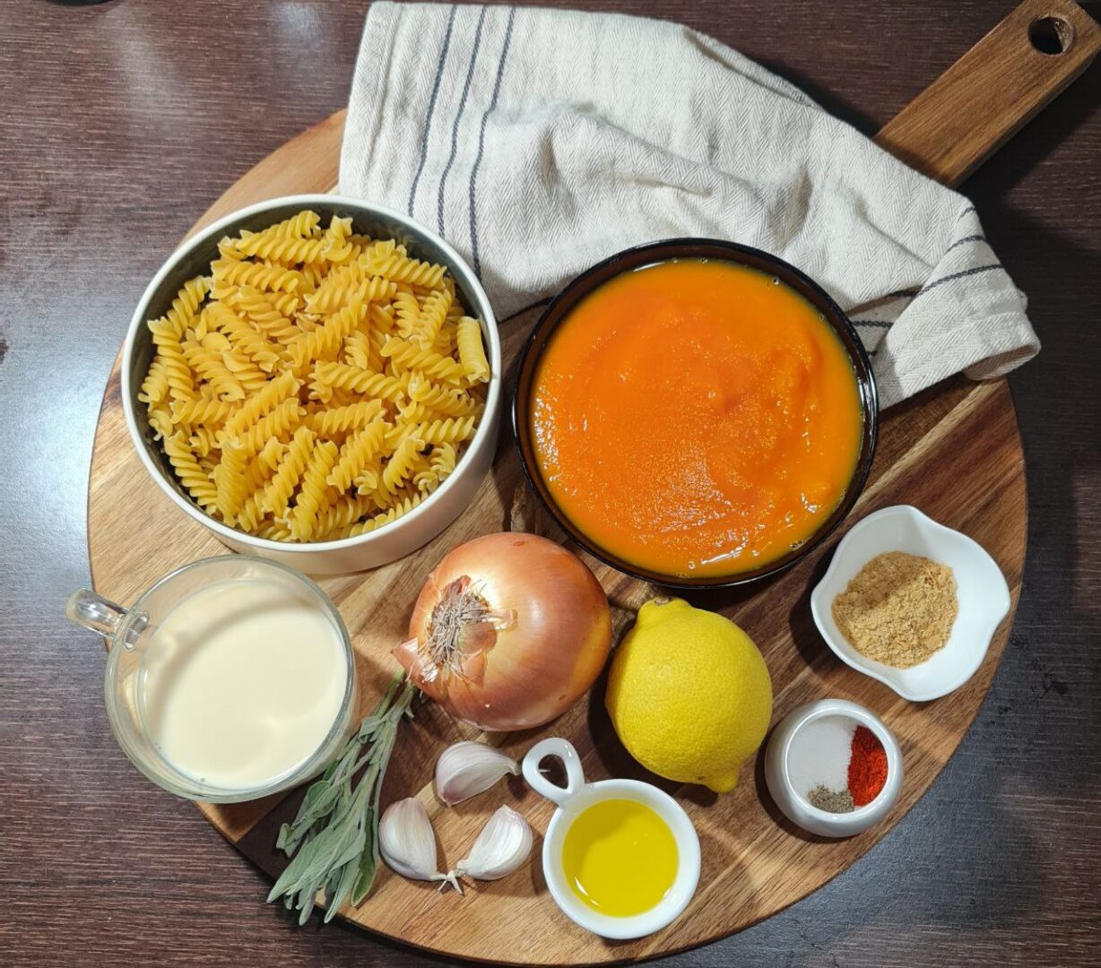 Ingredients for creamy vegan pumpkin pasta: fusilli, pumpkin puree, onion, garlic, lemon, sage, olive oil, and seasonings. Ingredients for creamy vegan pumpkin pasta laid out before cooking.