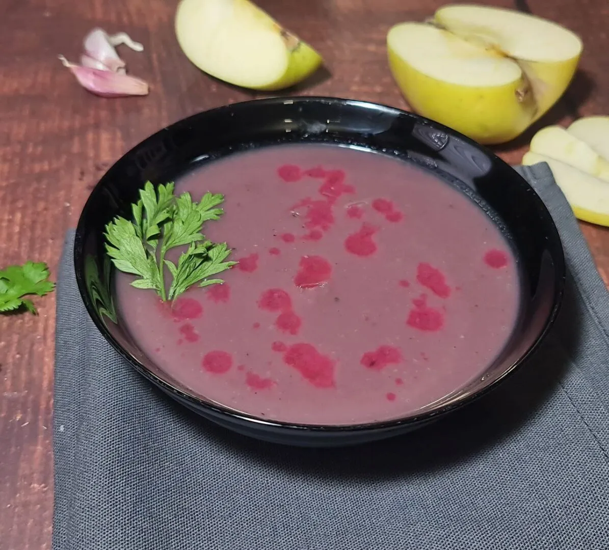 Finished bowl of vegan red cabbage soup with apple slices, garlic, and lemon on the side, garnished with fresh parsley.The finished vegan red cabbage soup, a healthy and vibrant dish for cold days.