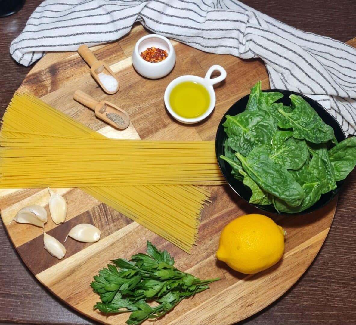 Flat lay of ingredients for vegan spaghetti aglio e olio with spinach, including spaghetti, garlic, spinach, olive oil, and lemon. Essential ingredients for vegan spaghetti aglio e olio with spinach laid out, including fresh spinach, spaghetti, garlic, olive oil, and lemon.