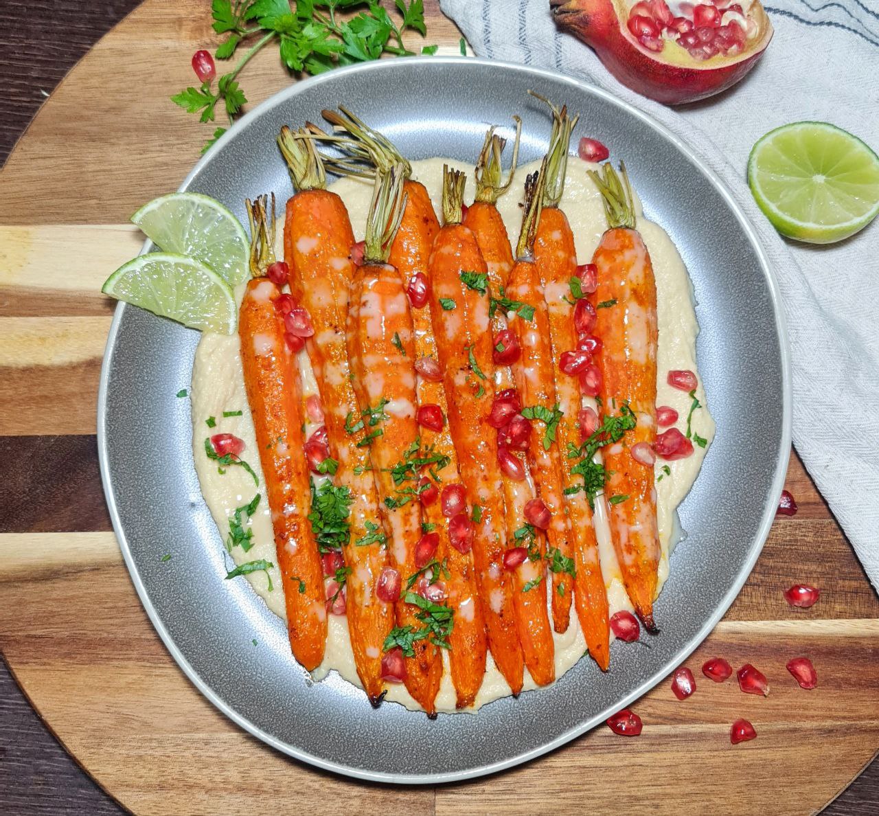 Roasted carrots served on a bed of creamy hummus, garnished with pomegranate seeds and fresh parsley. Whole roasted carrots with hummus, pomegranate, and parsley.