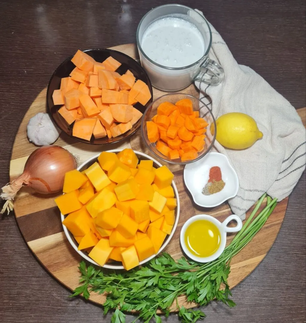 Ingredients for butternut squash and sweet potato soup including butternut squash, sweet potato, onion, garlic, carrots, coconut milk, and olive oil. Fresh ingredients for the butternut squash and sweet potato soup, ready to be prepped.