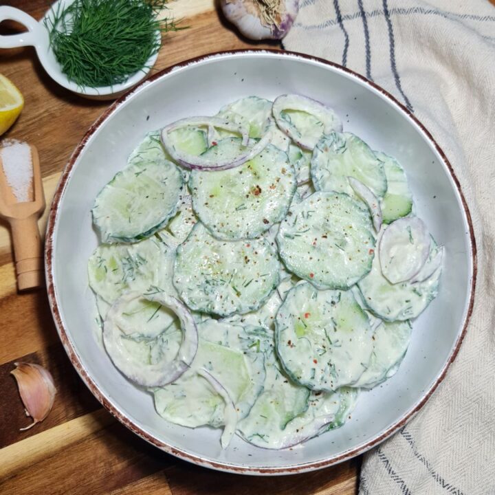 Sliced cucumbers and red onions in a bowl, topped with a creamy cashew dressing for cucumber salad preparation.