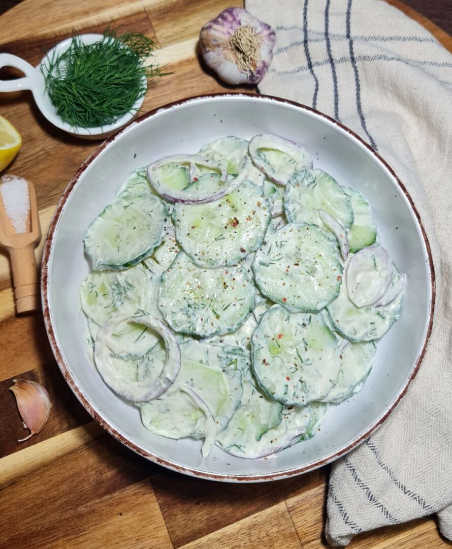 Sliced cucumbers and red onions in a bowl, topped with a creamy cashew dressing for cucumber salad preparation.