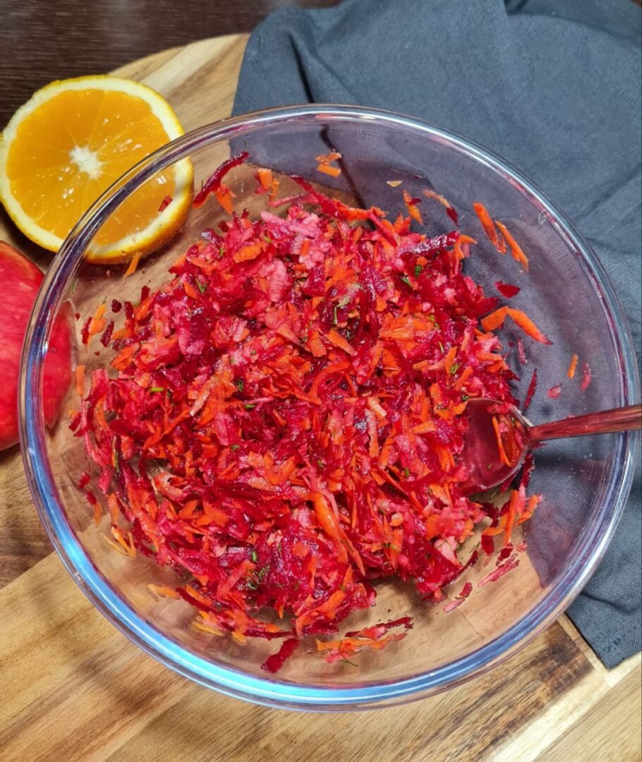 Bowl of freshly grated fall beetroot salad with orange and lemon slices in the background. Preparing the fall beetroot salad with a blend of vibrant grated vegetables and fresh citrus.