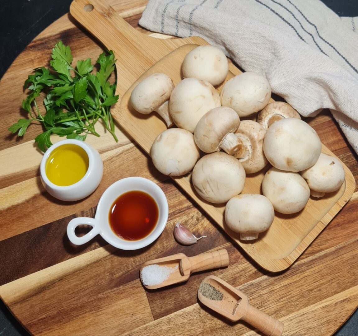 Fresh mushrooms, olive oil, soy sauce, garlic, salt, and pepper on a wooden board. Key ingredients for making the best sautéed mushrooms, including fresh mushrooms, olive oil, soy sauce, and garlic.