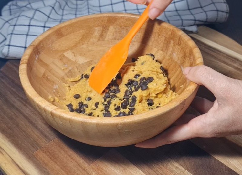  Mixing vegan pumpkin chocolate chip cookie dough in a wooden bowl with a spatula. Mixing vegan pumpkin chocolate chip cookie dough filled with chocolate chips.