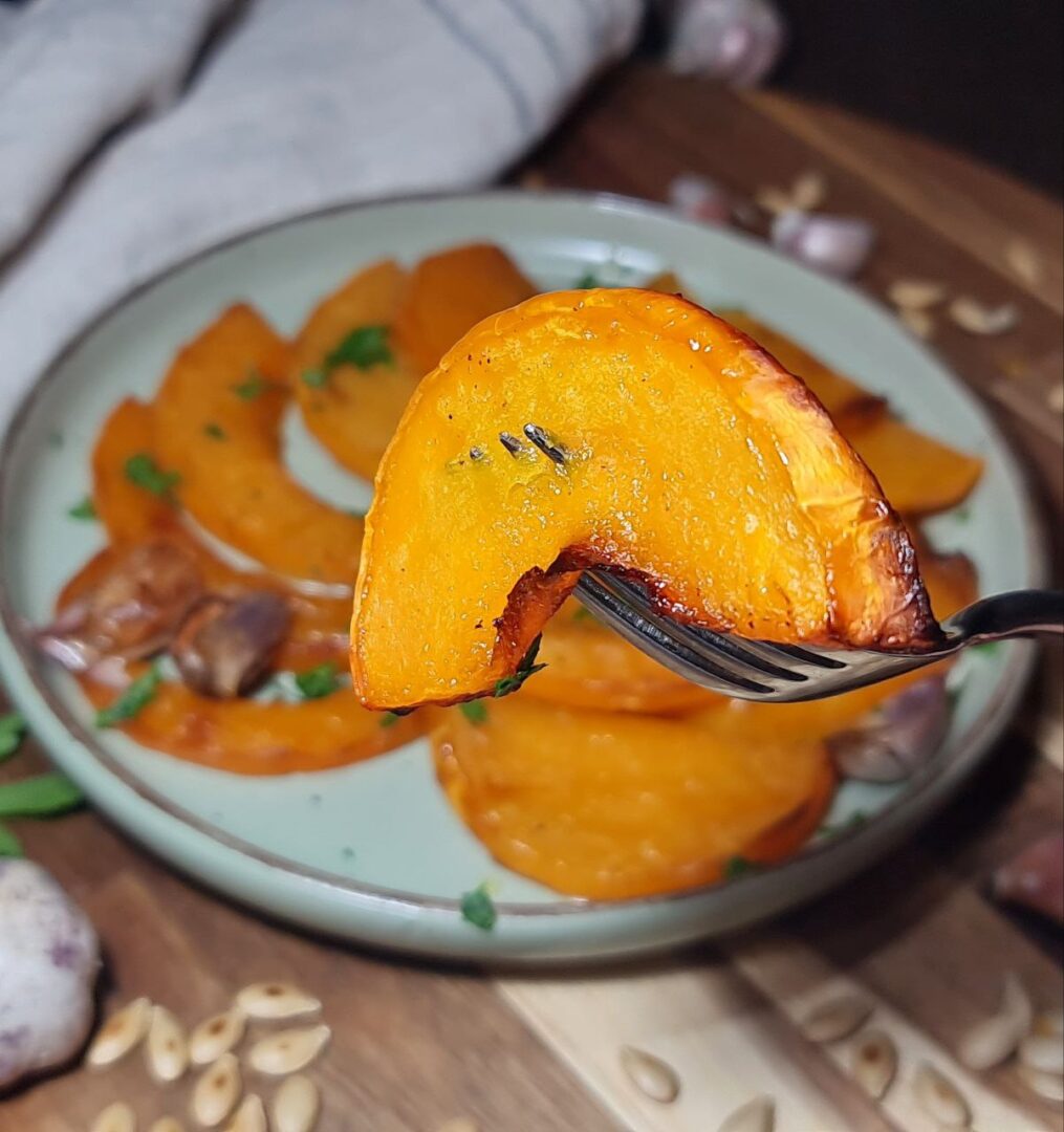 Close-up of a roasted butternut squash slice on a fork. Roasted butternut squash slice served with garlic and herbs.