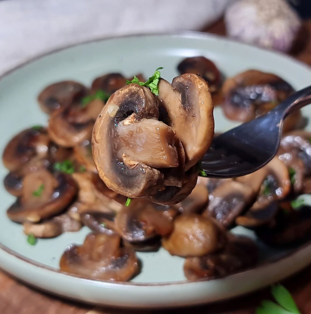 Close-up of a fork holding a piece of sautéed mushroom garnished with parsley. A delicious close-up of sautéed mushrooms, perfectly tender and garnished with fresh parsley.