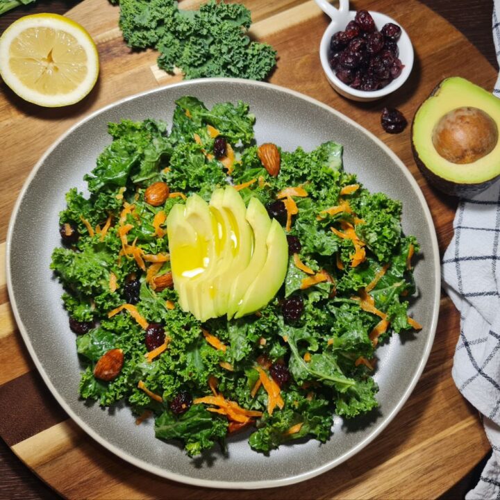 a plate of simple kale salad with avocado and nuts