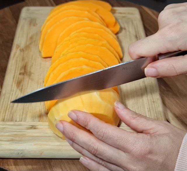  Hands slicing butternut squash into even pieces on a cutting board. Slicing butternut squash into perfect rounds for roasting.