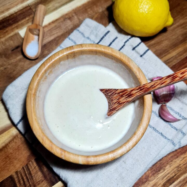 a bowl of white liquid tahini dressing recipe with a wooden spoon