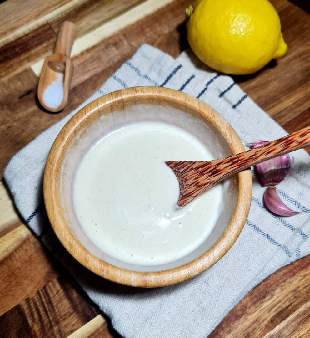 a bowl of white liquid tahini dressing recipe with a wooden spoon