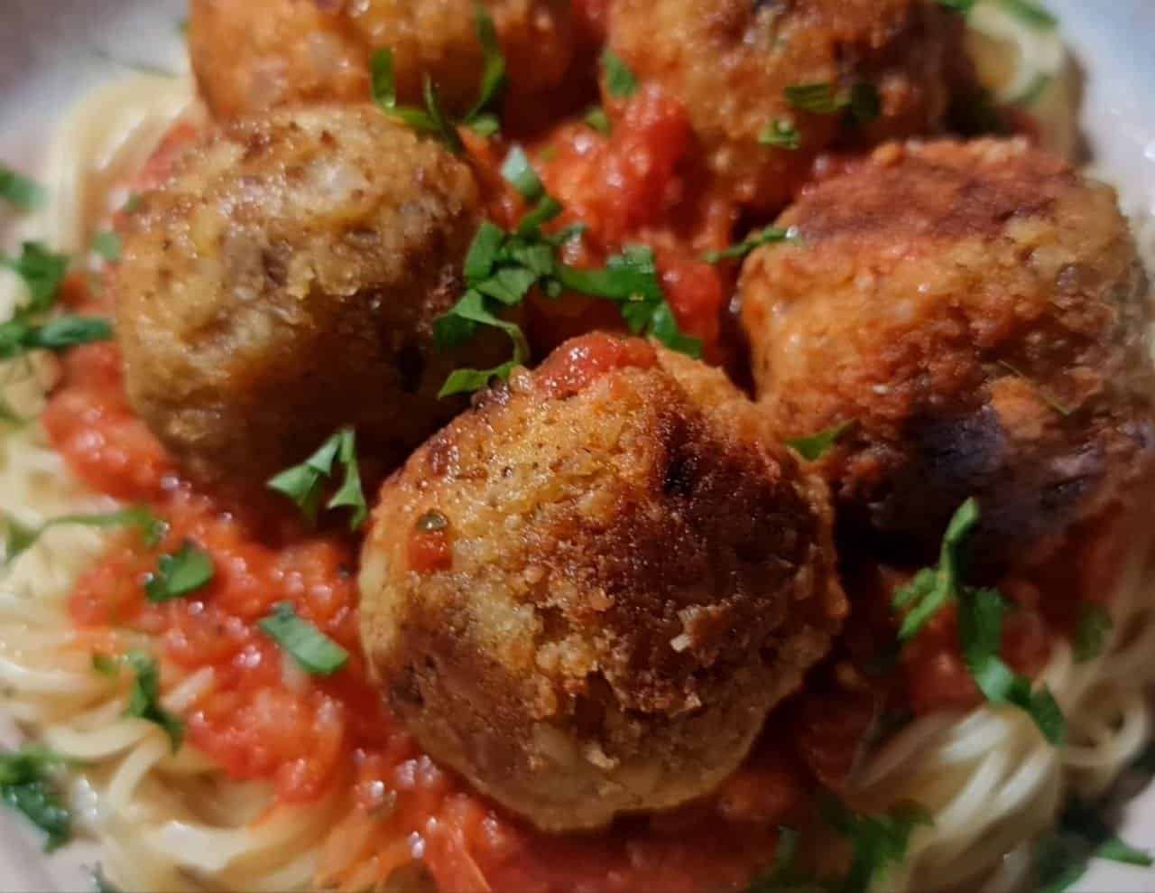 A close-up of vegan chickpea meatballs served over spaghetti with tomato sauce and garnished with fresh herbs.