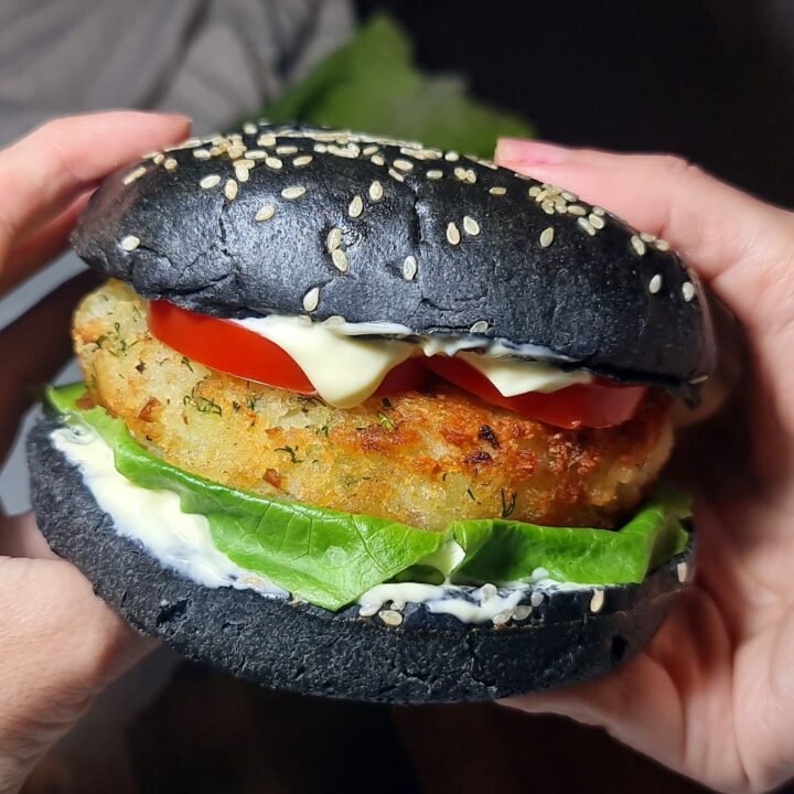 Vegan potato burger with charcoal bun, lettuce, tomato, and vegan mayonnaise. Delicious vegan potato burger with a crispy patty, fresh lettuce, tomato, and vegan mayo on a charcoal bun.