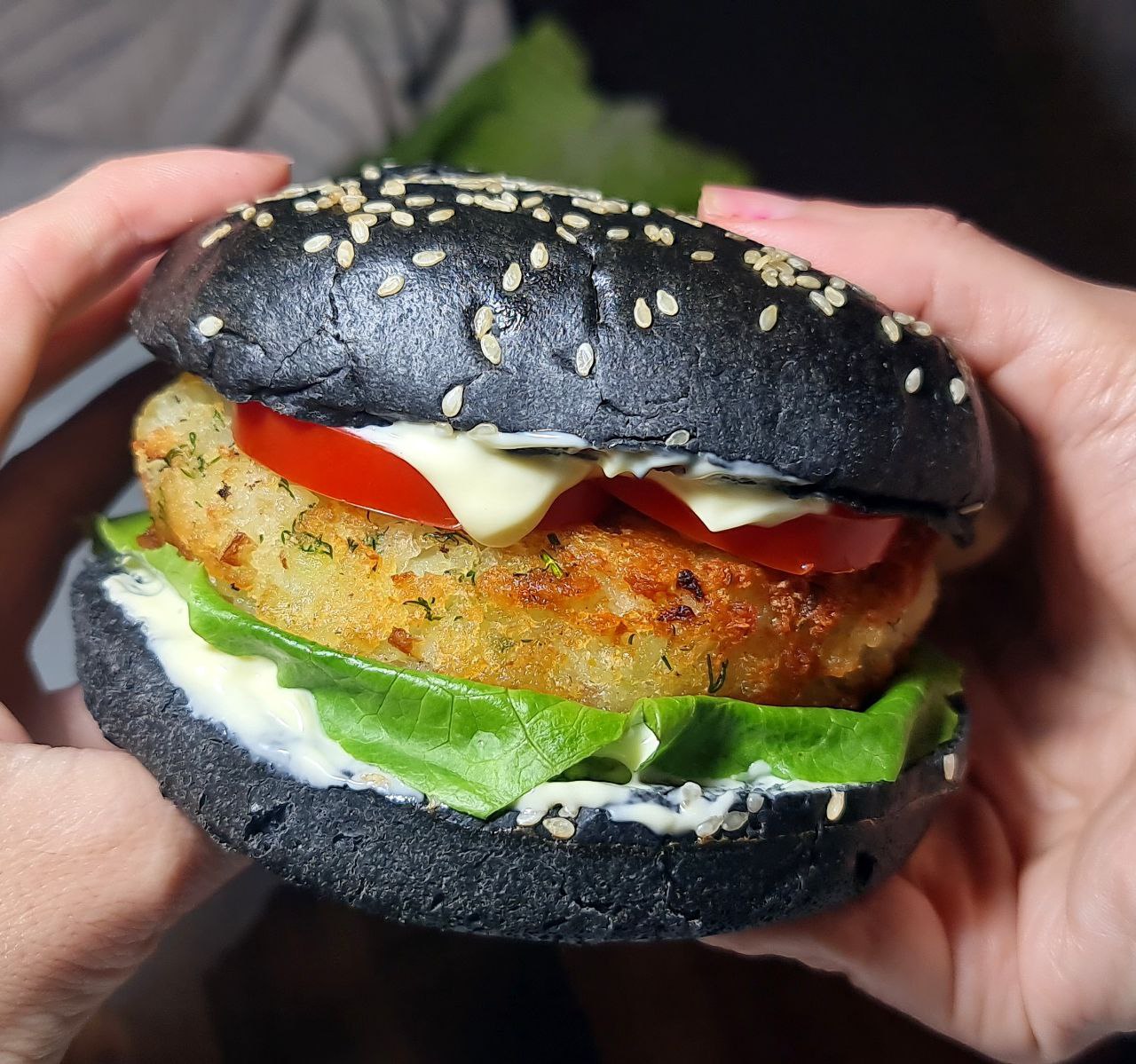 Vegan potato burger with charcoal bun, lettuce, tomato, and vegan mayonnaise. Delicious vegan potato burger with a crispy patty, fresh lettuce, tomato, and vegan mayo on a charcoal bun.