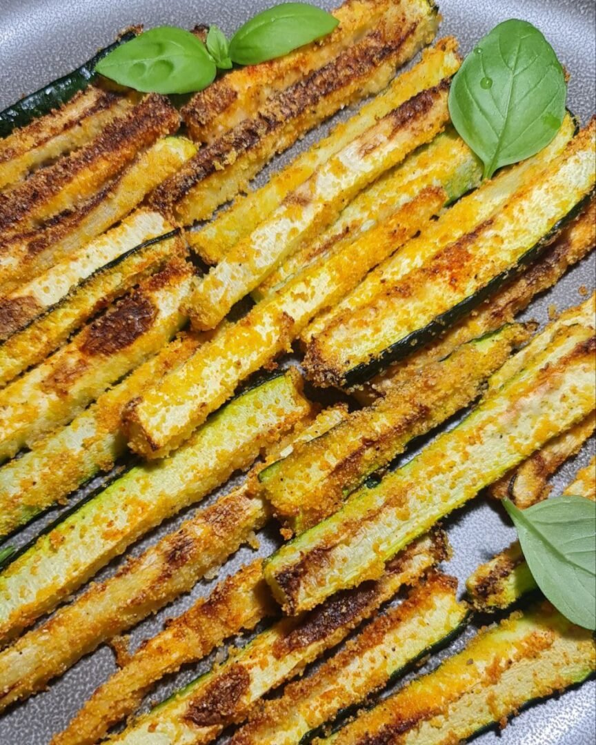 Close-up view of crispy vegan zucchini sticks garnished with fresh basil. Deliciously crispy vegan zucchini sticks served with fresh basil.