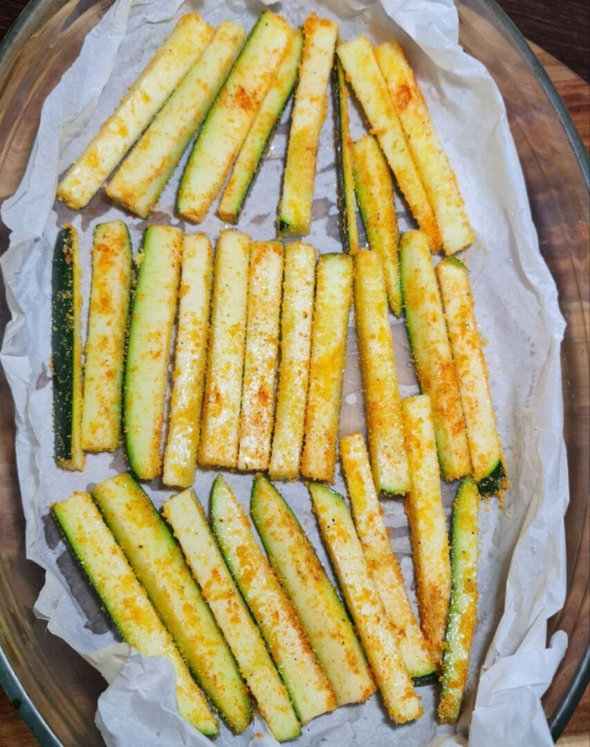 Seasoned vegan zucchini sticks arranged on a baking tray lined with parchment paper. Vegan zucchini sticks ready to be baked to crispy perfection.