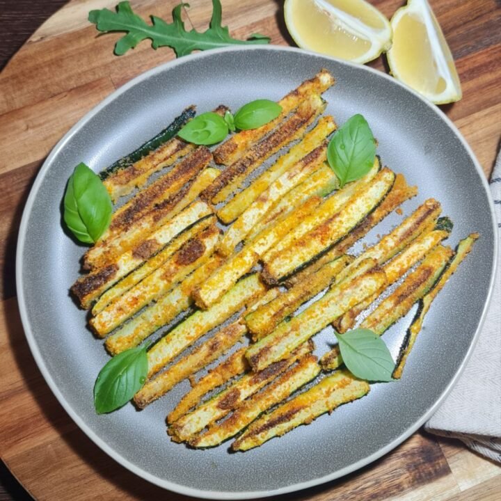 Vegan zucchini sticks served on a grey plate with basil and lemon wedges. Vegan zucchini sticks served with fresh basil and lemon for a burst of flavor.