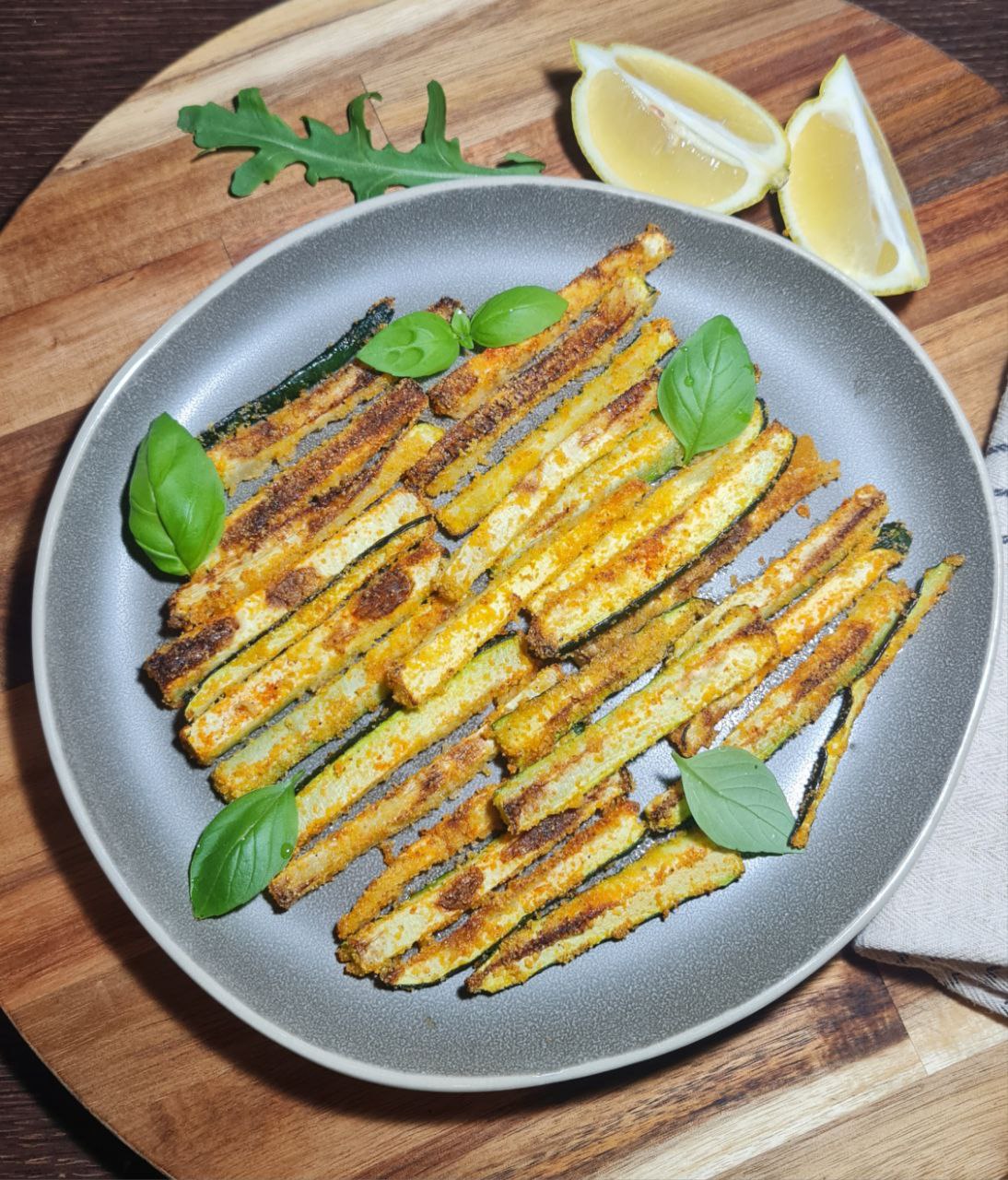 Vegan zucchini sticks served on a grey plate with basil and lemon wedges. Vegan zucchini sticks served with fresh basil and lemon for a burst of flavor.