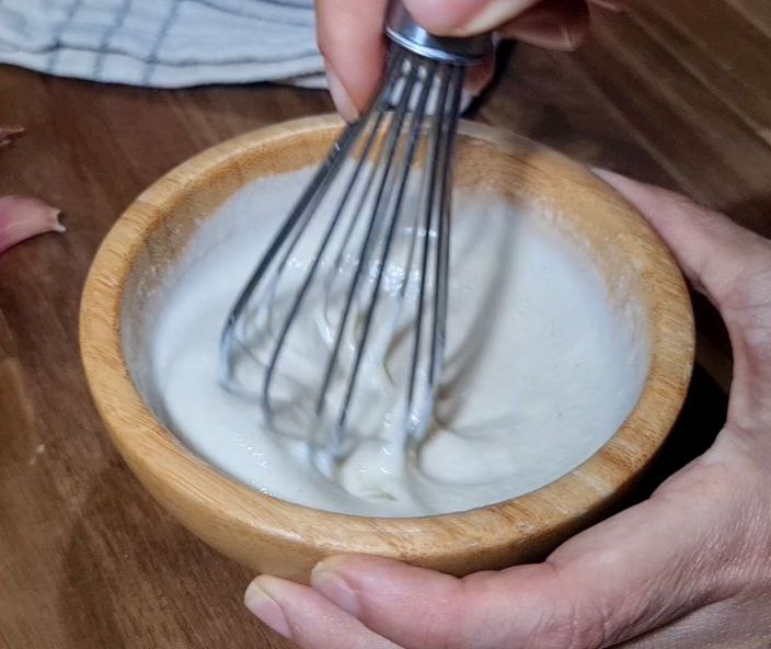 Hand whisking tahini dressing in a wooden bowl. Whisking tahini dressing to create a creamy consistency.