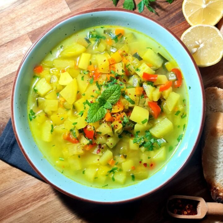 A bowl of golden vegetable soup garnished with fresh parsley and mint, served with lemon and crusty bread. A warm bowl of golden vegetable soup, perfect for cozy evenings.