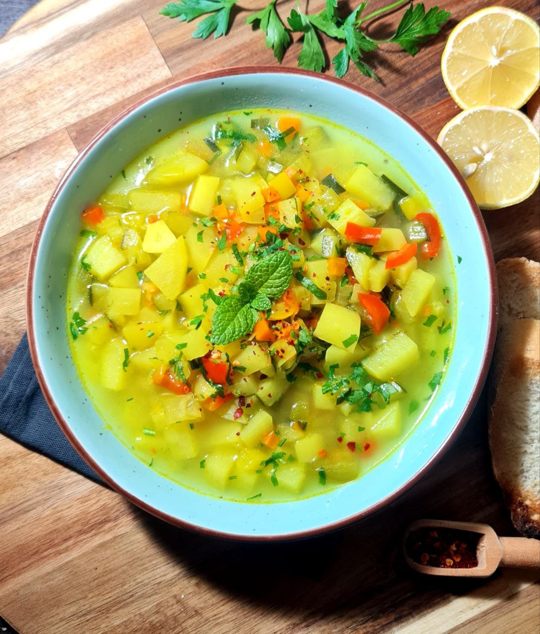 A bowl of golden vegetable soup garnished with fresh parsley and mint, served with lemon and crusty bread. A warm bowl of golden vegetable soup, perfect for cozy evenings.