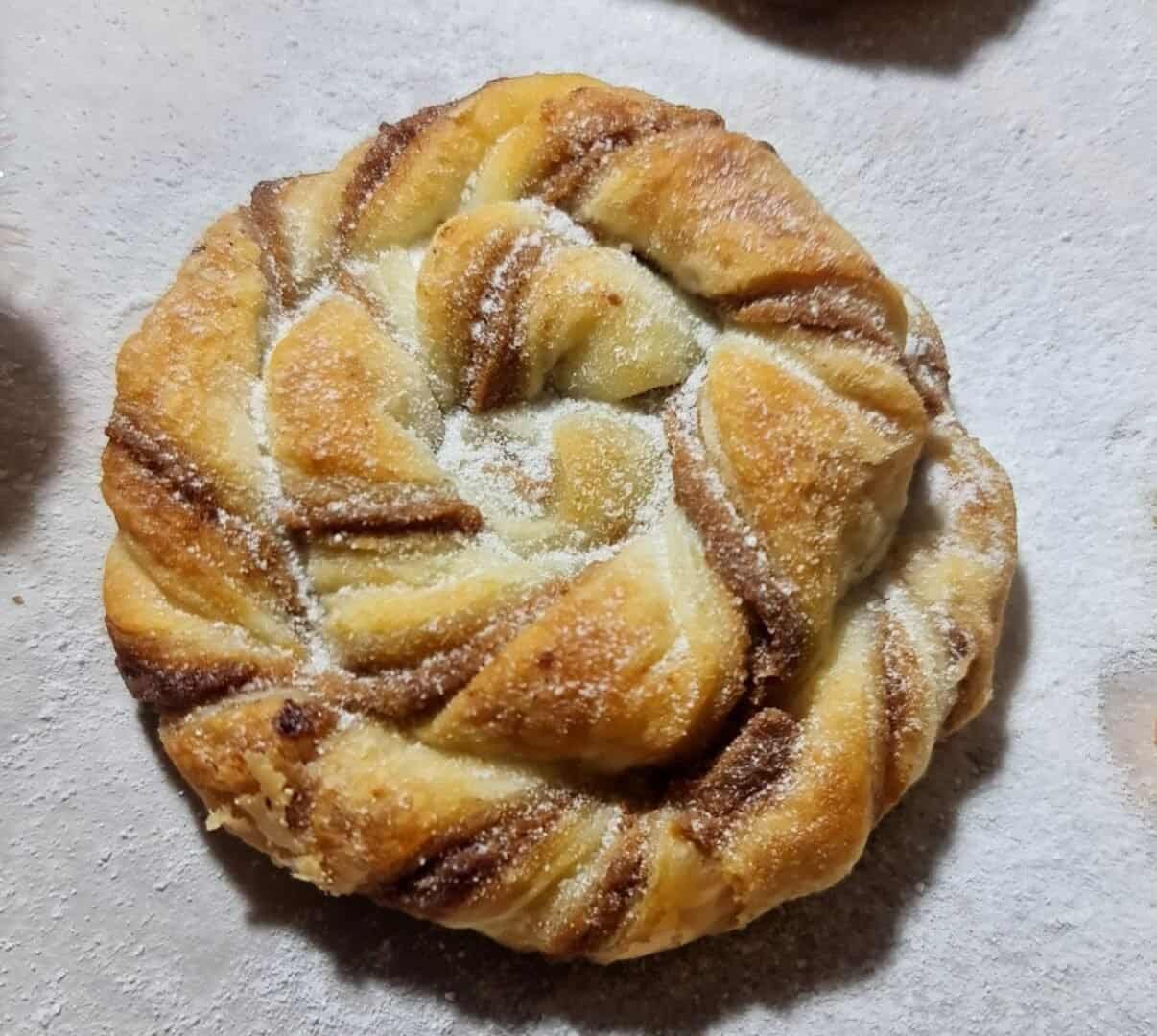 Close-up of a golden-brown baked Biscoff swirl dusted with powdered sugar.