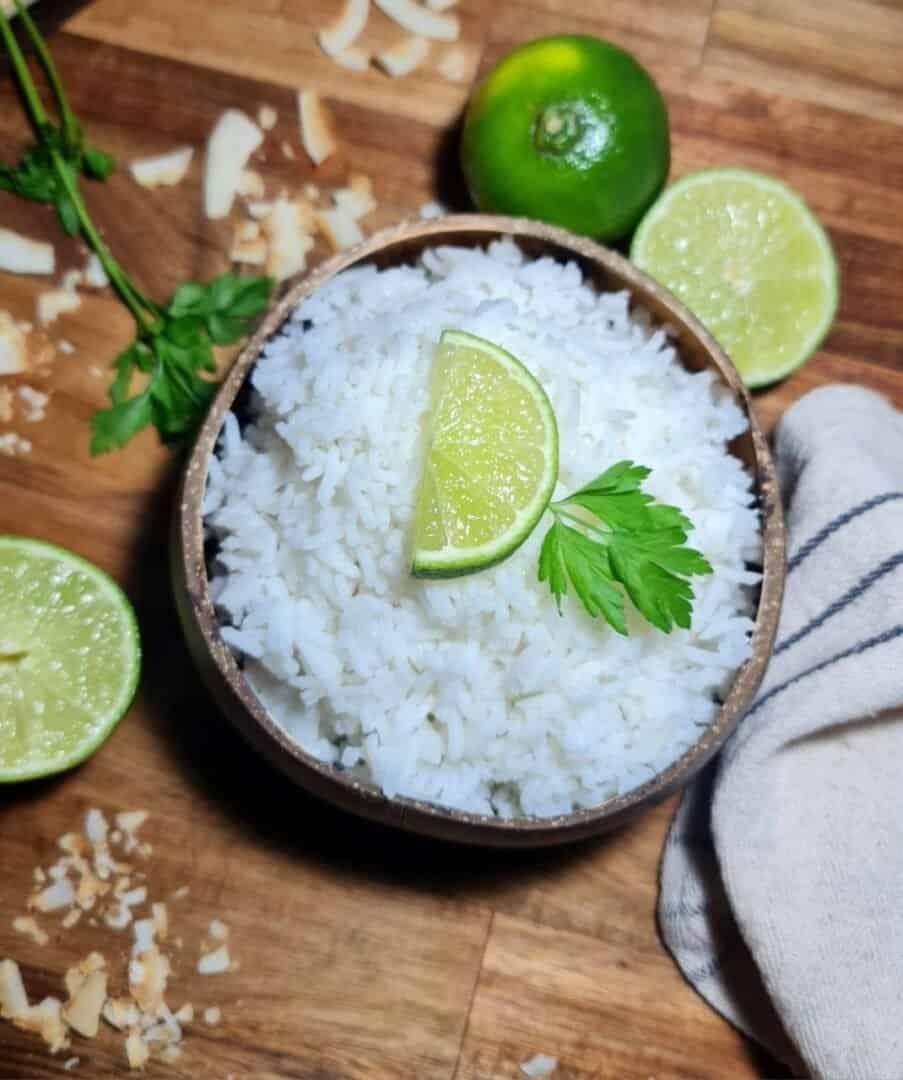 Coconut rice garnished with fresh herbs and lime wedges in a bowl.