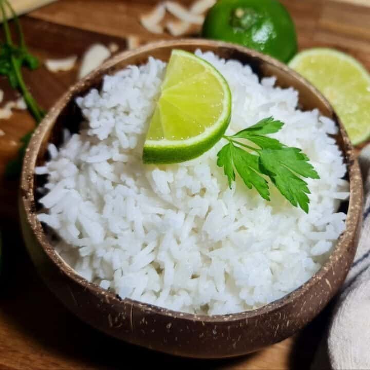 A bowl of coconut rice garnished with a lime wedge and a sprig of parsley.