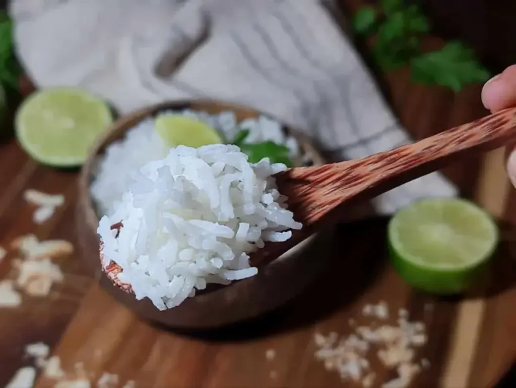 Close-up shot of fluffy, fragrant homemade coconut rice scooped on a wooden spoon showcasing its texture.

