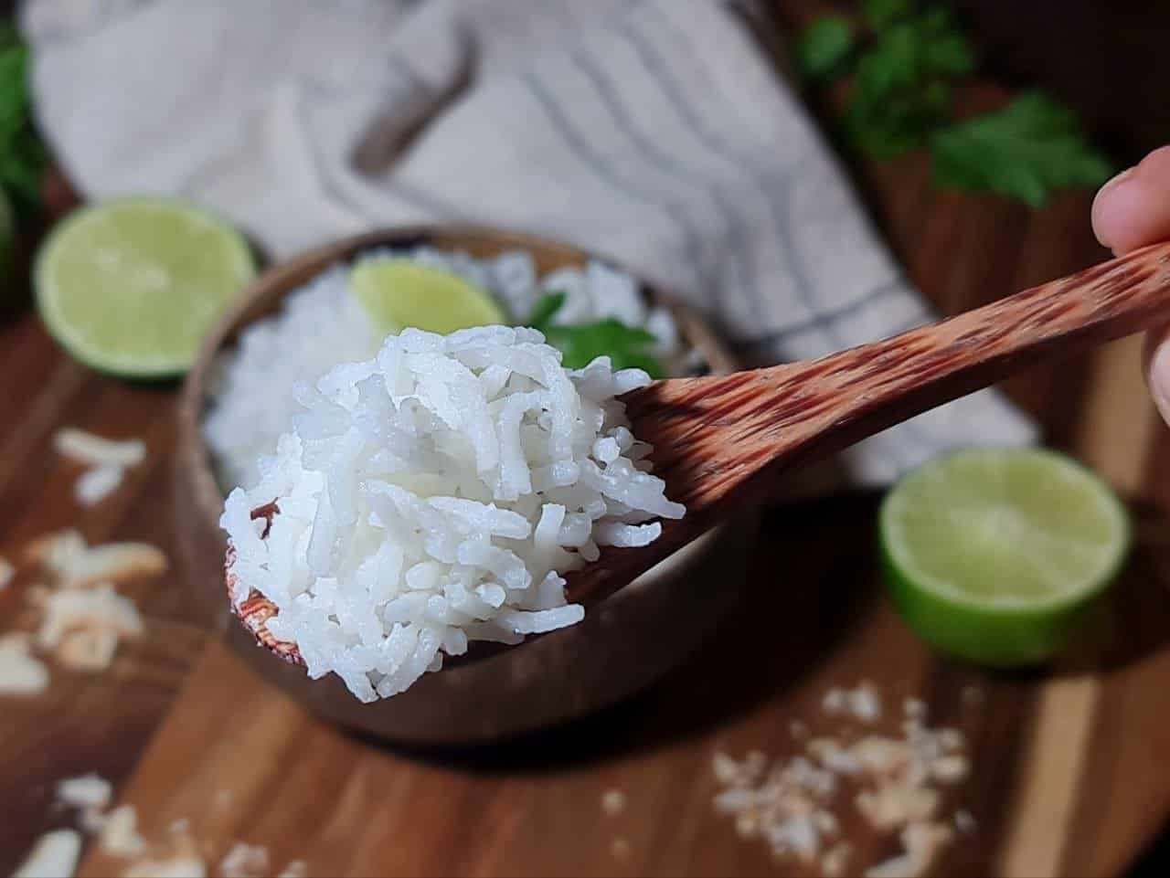 Coconut rice cooking in a pot with a wooden spoon stirring the mixture. 