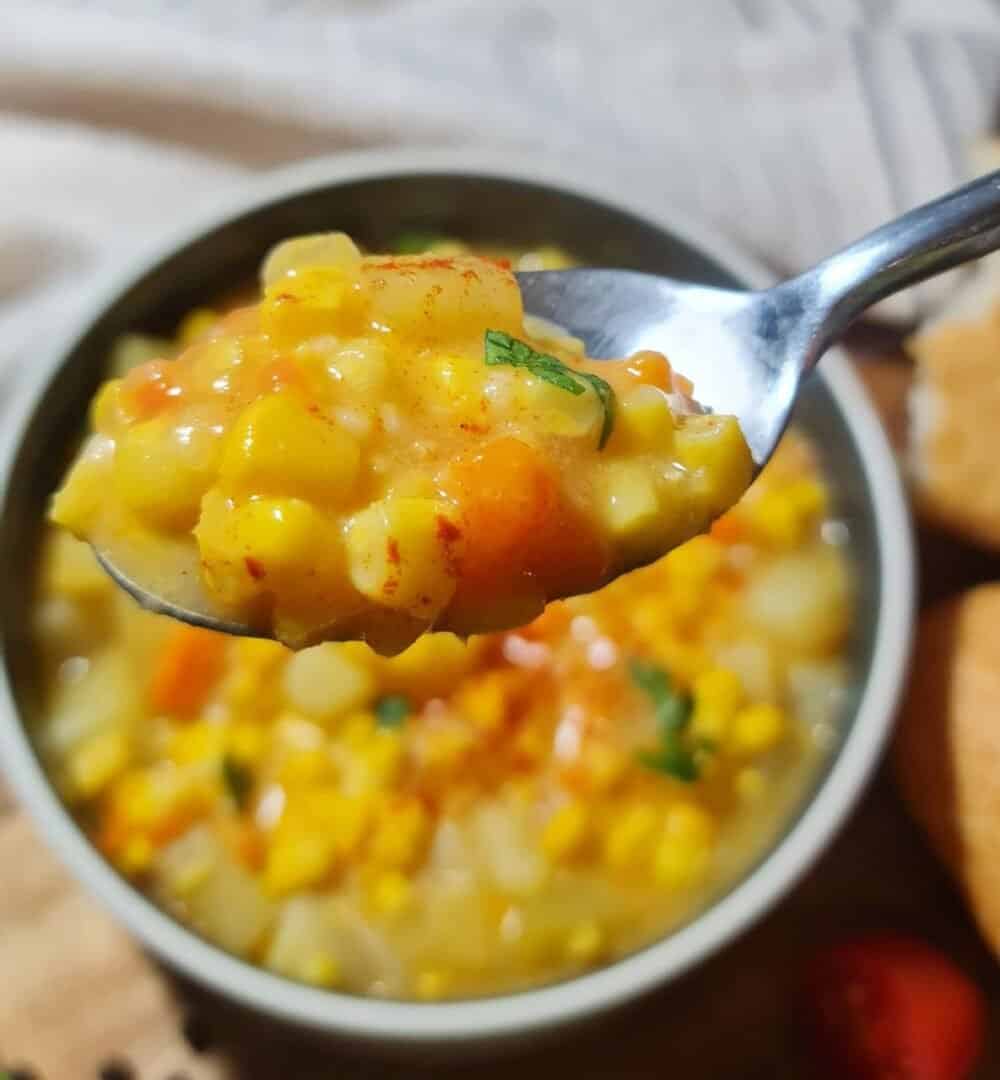 Close-up of a spoonful of creamy corn chowder with visible corn kernels, diced potatoes, and carrots. A spoonful of delicious and creamy corn chowder. 