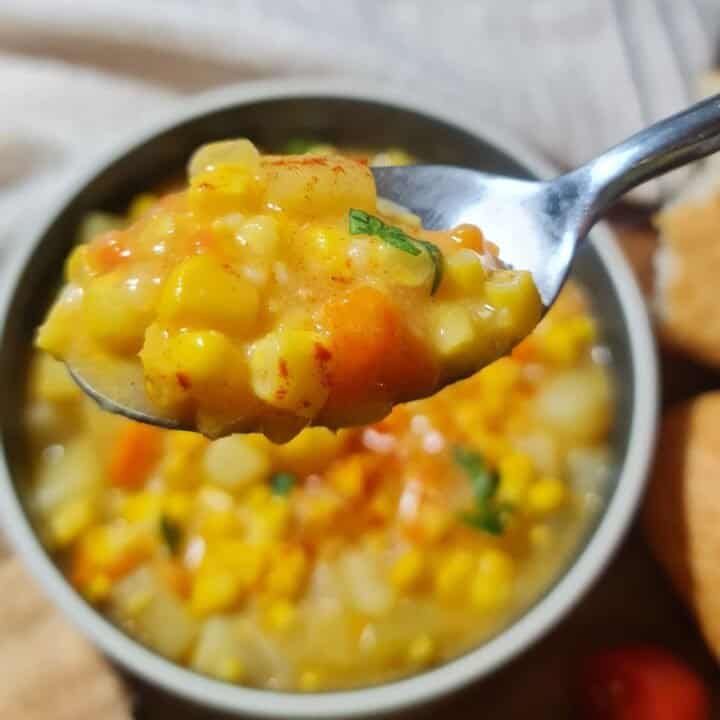 Close-up of a spoonful of creamy corn chowder with visible corn kernels, diced potatoes, and carrots. A spoonful of delicious and creamy corn chowder.