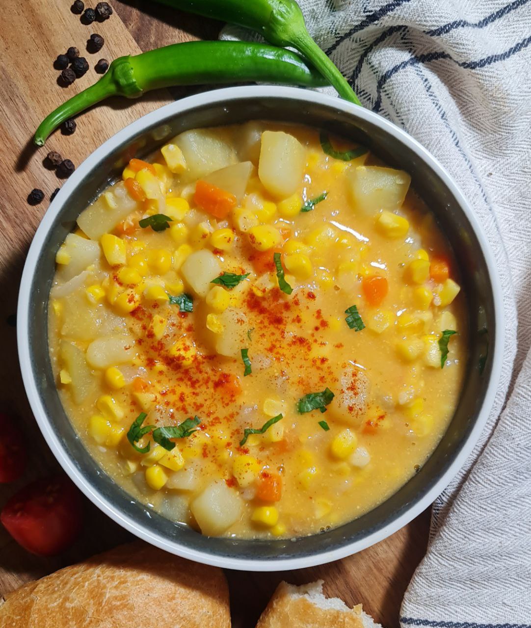 A bowl of creamy corn chowder garnished with fresh herbs, served with a slice of bread. A warm and comforting bowl of creamy corn chowder.