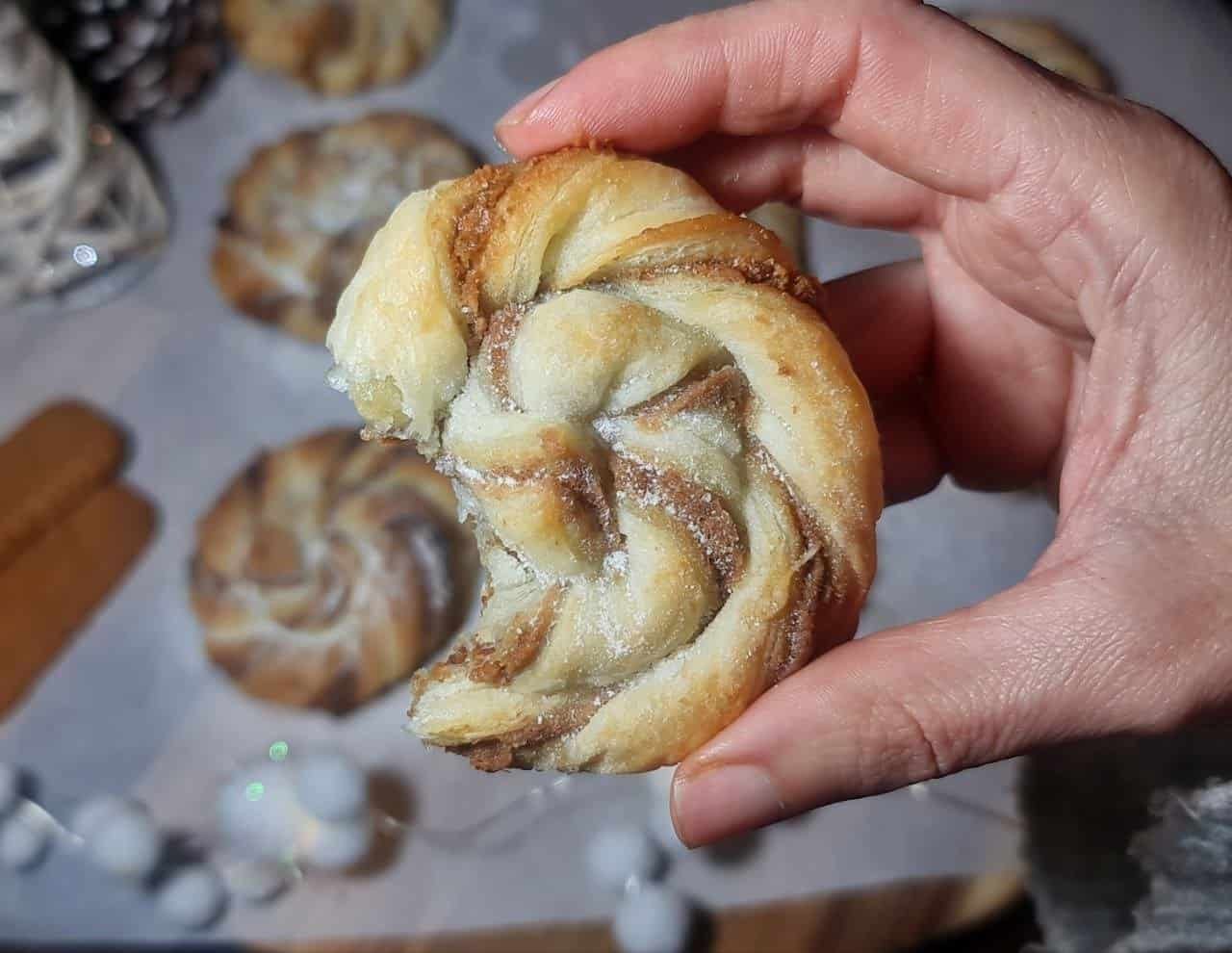 A hand holding a Biscoff swirl with a bite taken out, showcasing the flaky layers.  Enjoying a delicious Biscoff swirl with visible flaky layers and rich filling.