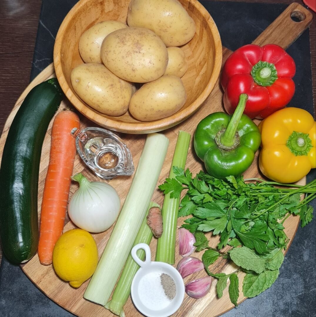 Fresh vegetables and herbs for making golden vegetable soup, including potatoes, peppers, zucchini, carrot, onion, and spices. Fresh, colorful ingredients for a wholesome golden vegetable soup.