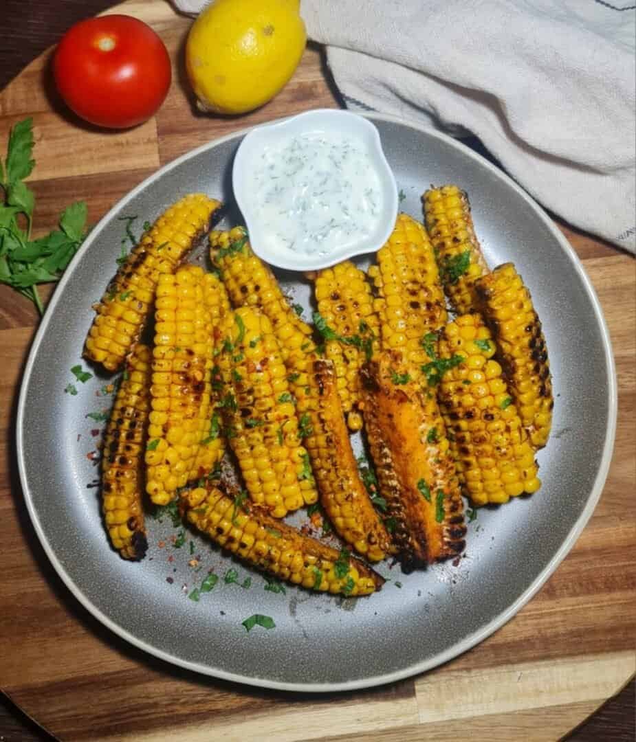  Close-up of grilled corn ribs being dipped into a creamy white sauce with green herbs. Grilled corn ribs being dipped into a creamy herb sauce, perfect for a delicious snack.